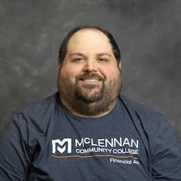 Smiling man in a McLennan Community College T-shirt against a gray studio backdrop.